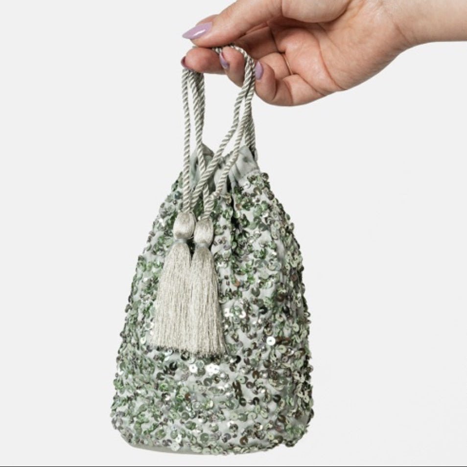 Hand holding a decorative bag with sequins and tassels on a white background