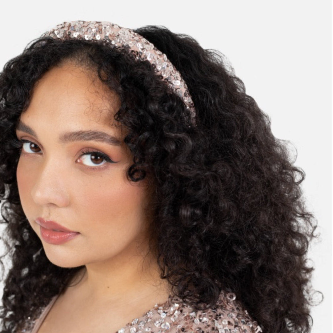 Woman wearing a sparkling headband and sequin top against a plain background