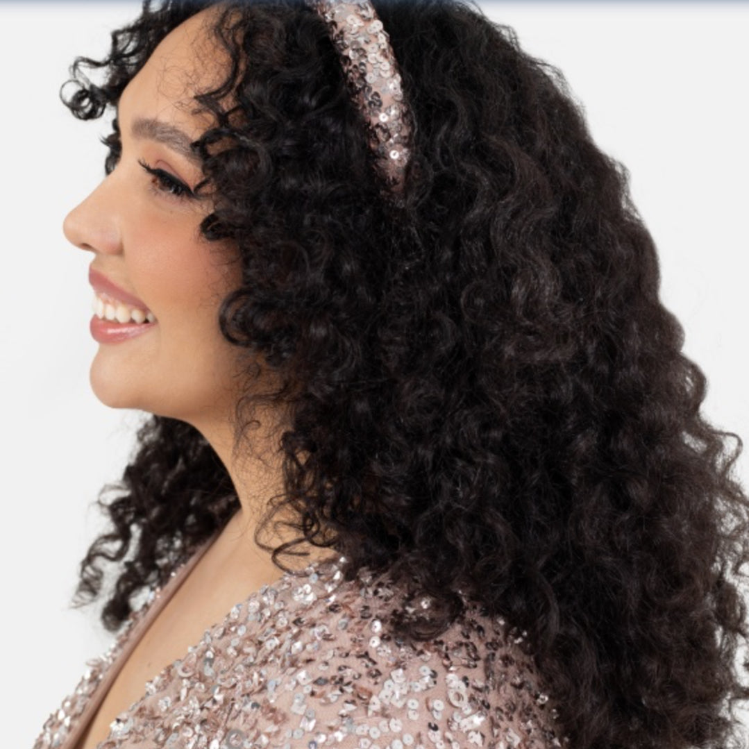 Woman with curly hair wearing a sparkly headband and sequin top on a white background