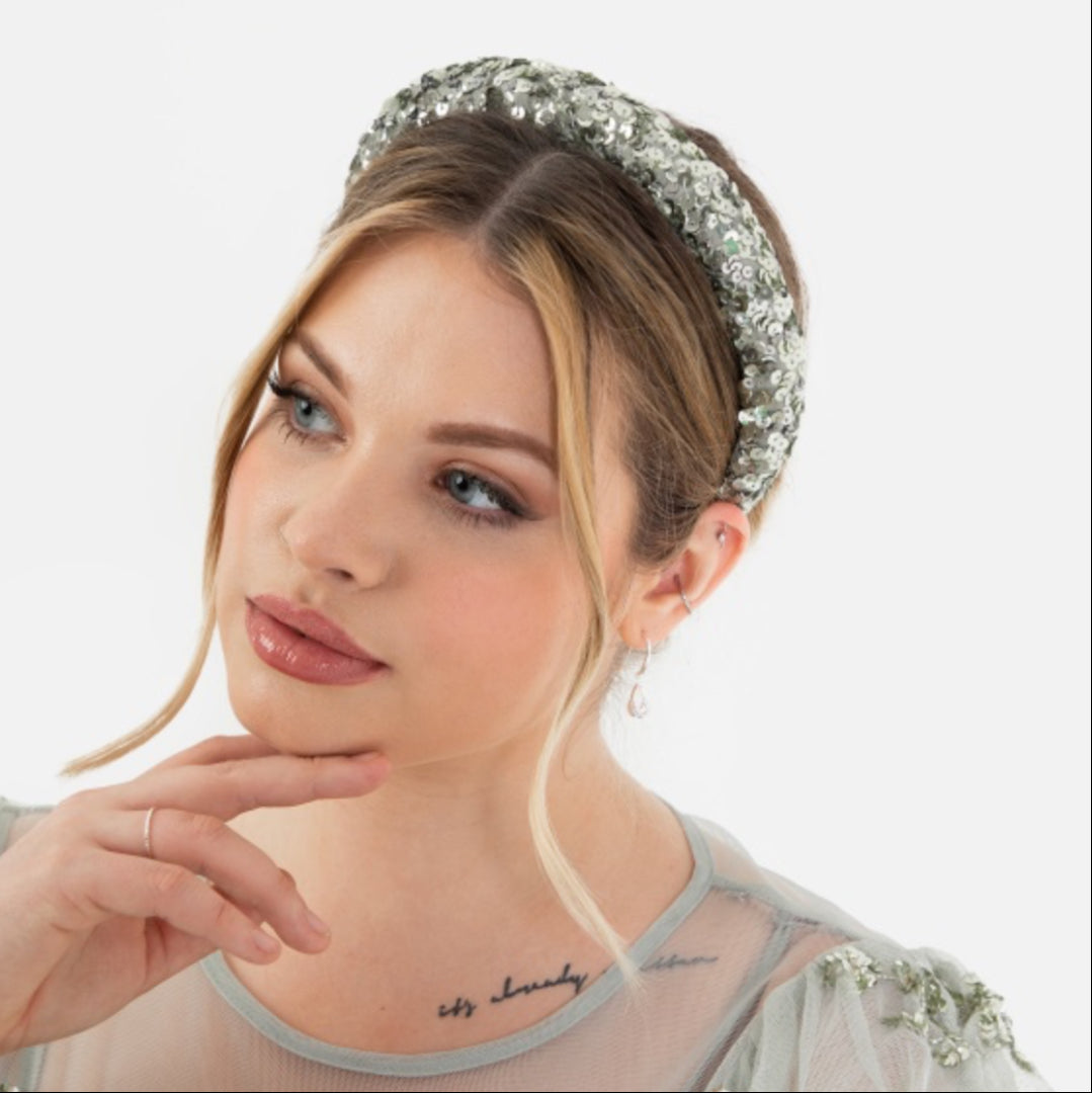 Woman wearing a sparkling headband and dress with floral embellishments on a white background